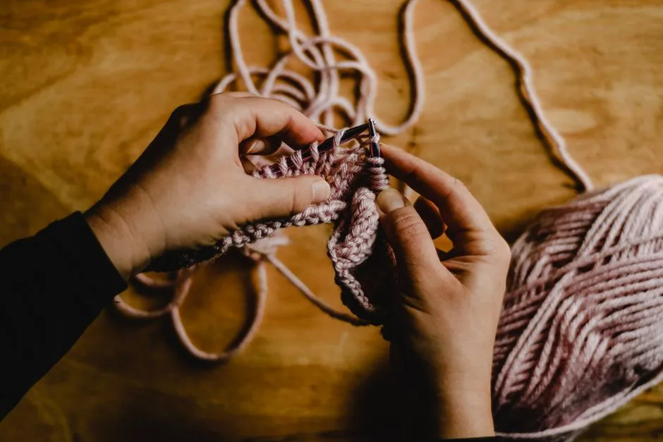 Close-up of hands knitting a swatch with pale pink wool and a ball of yarn nearby