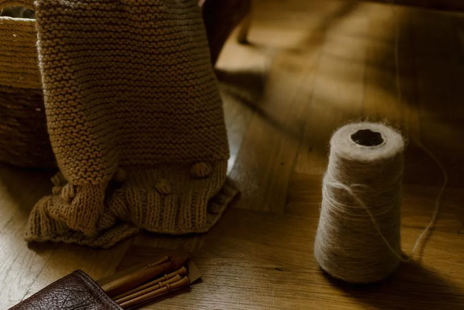 A handmade knitted piece resting in a wicker basket next to knitting needles and a spool of thread